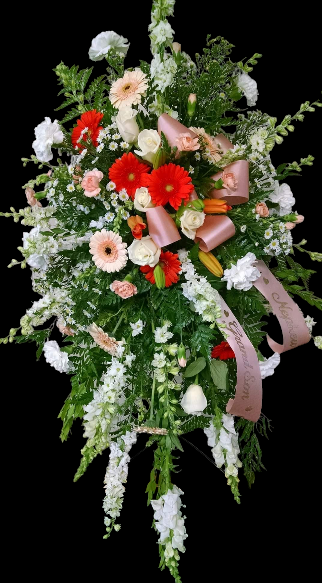 Floral spray with red, peach, and white flowers, accented with greenery and a ribbon.