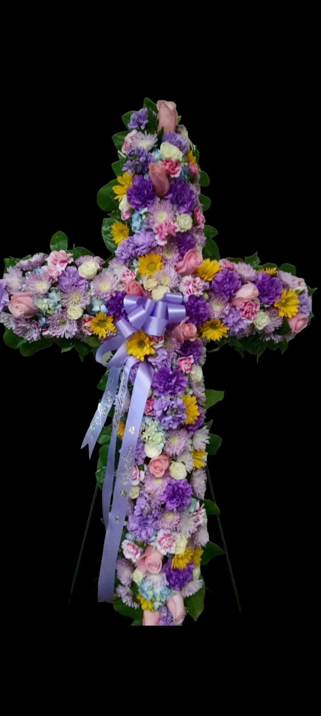 Floral cross composed of purple, yellow, and pink flowers against a black background.