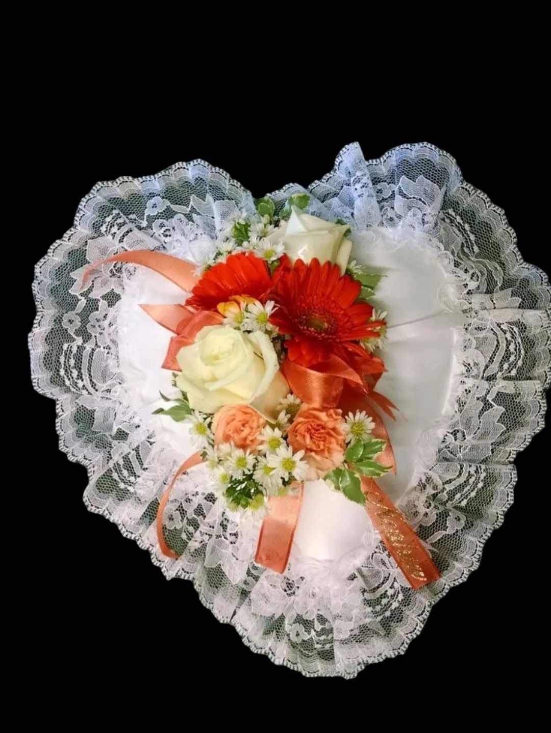 Heart-shaped white pillow with lace trim, adorned with orange and white flowers, and peach ribbon.