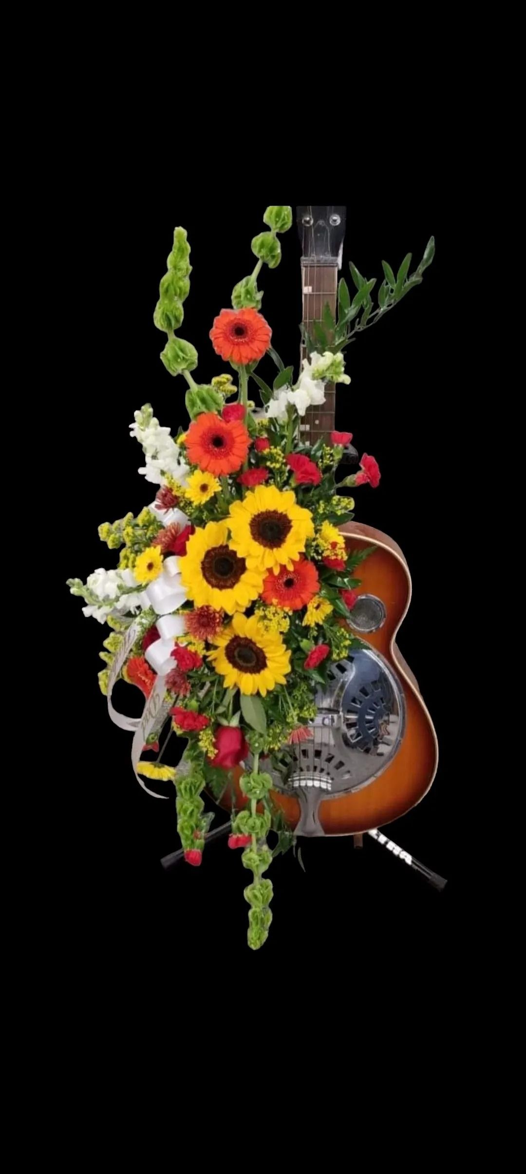 Acoustic guitar decorated with a floral arrangement of sunflowers, daisies, and other colorful blooms.