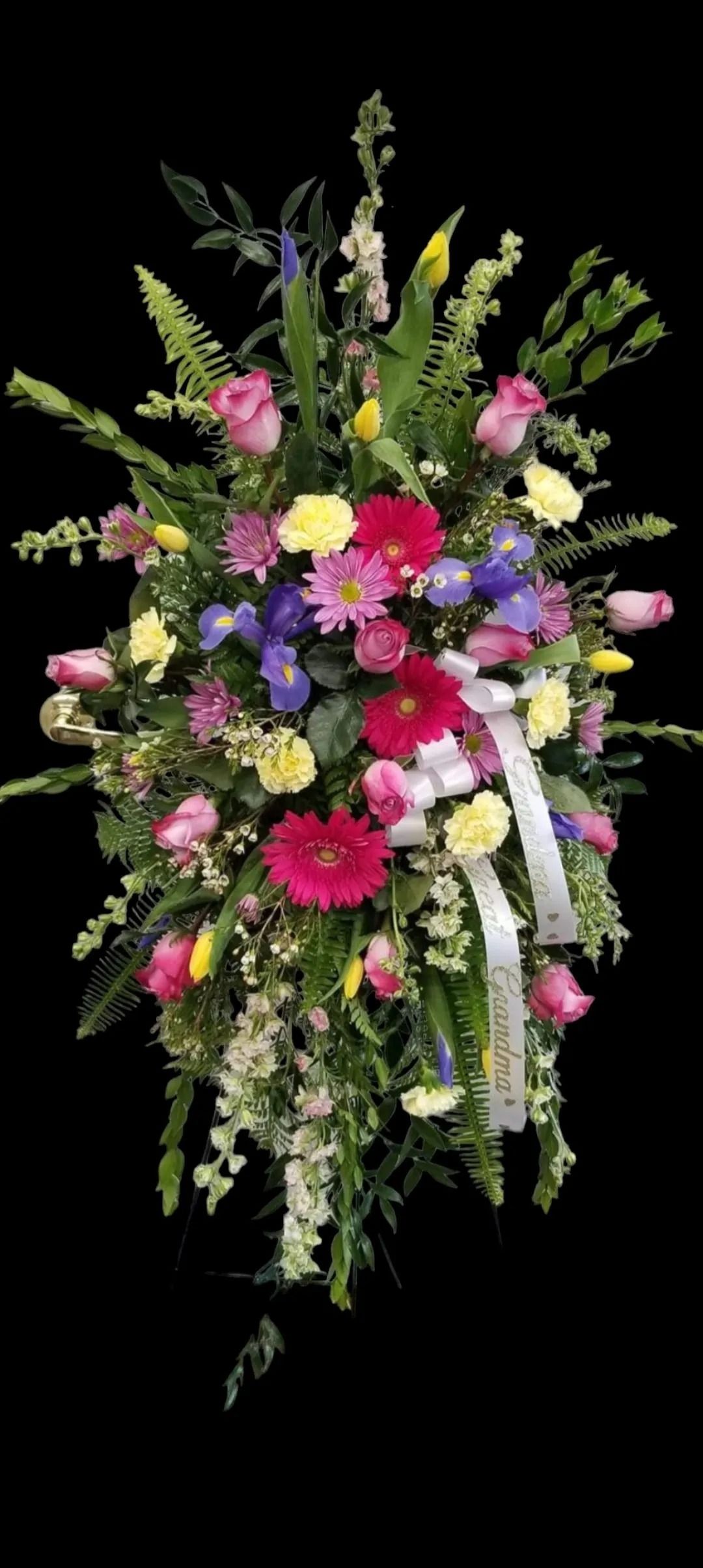 A colorful floral arrangement with various blooms, including roses, gerberas, and ribbons, against a black backdrop.