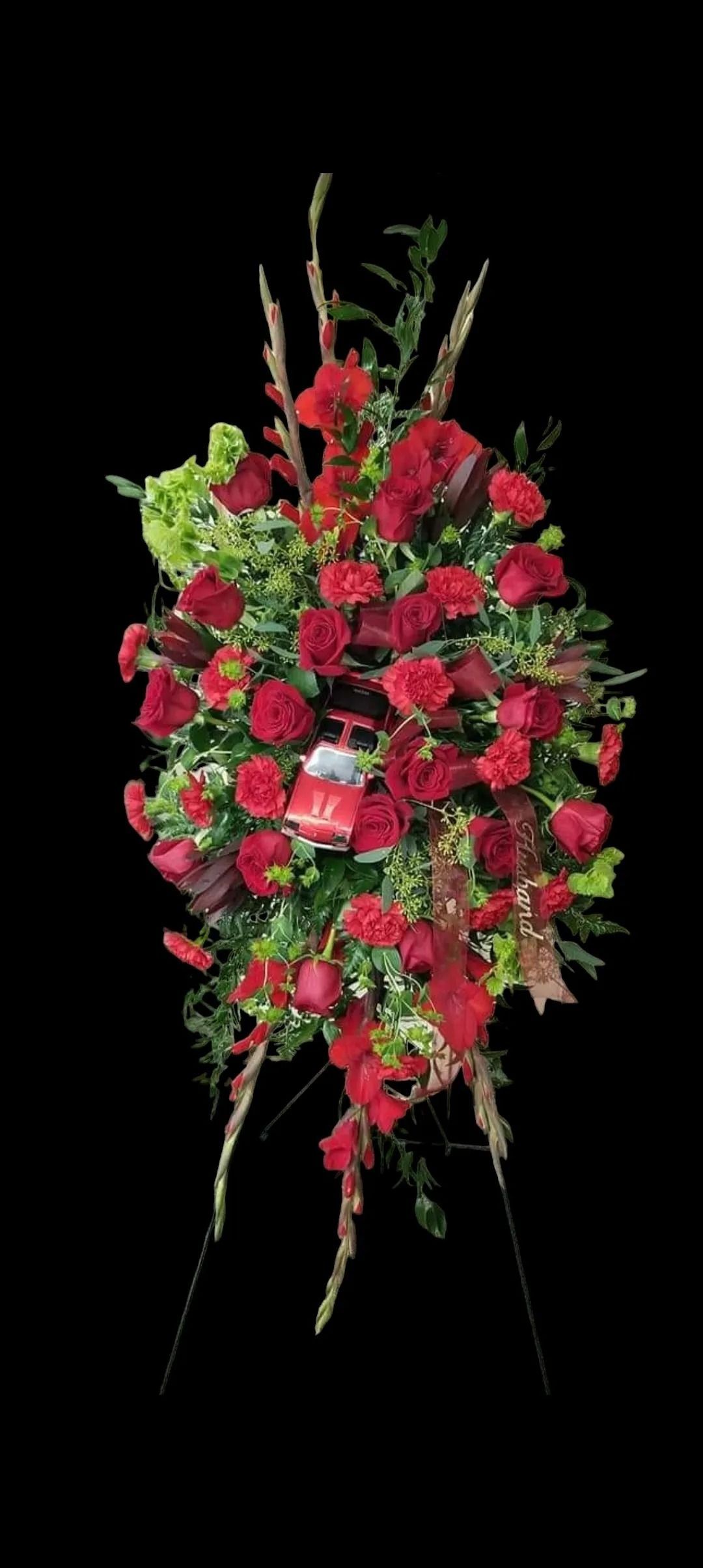 Red rose floral arrangement on a stand with a black background.