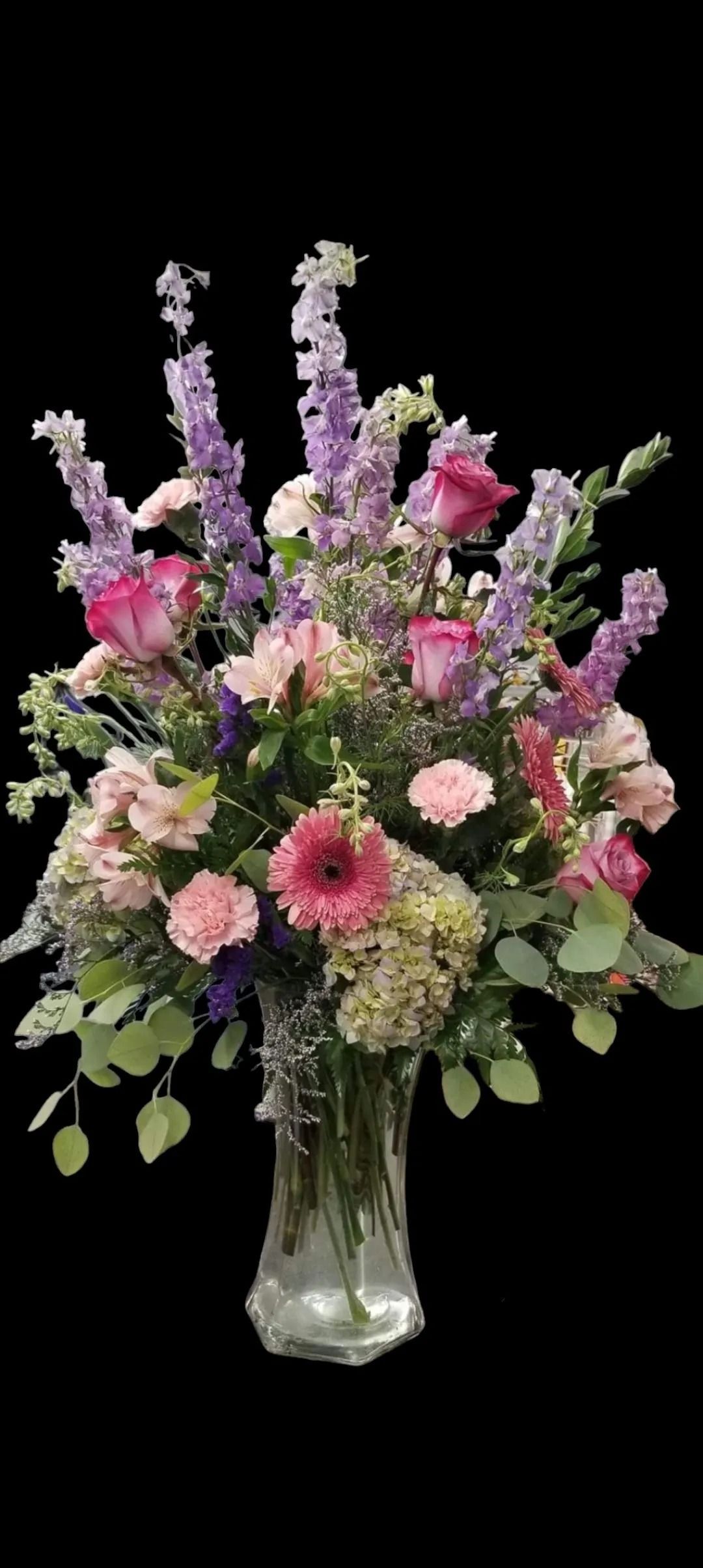 Vase of mixed flowers in shades of pink, purple, and green against a black background.