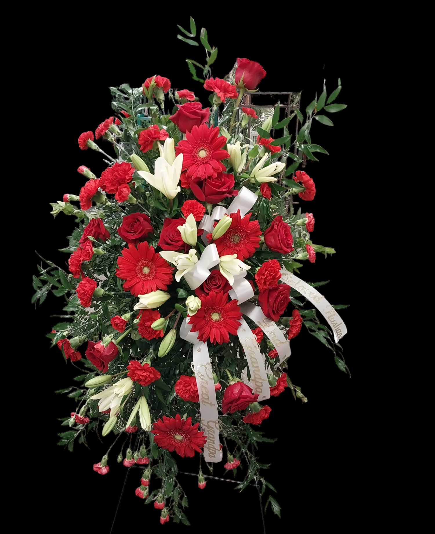 Red and white floral arrangement, likely a memorial piece, with a white ribbon, against a black background.