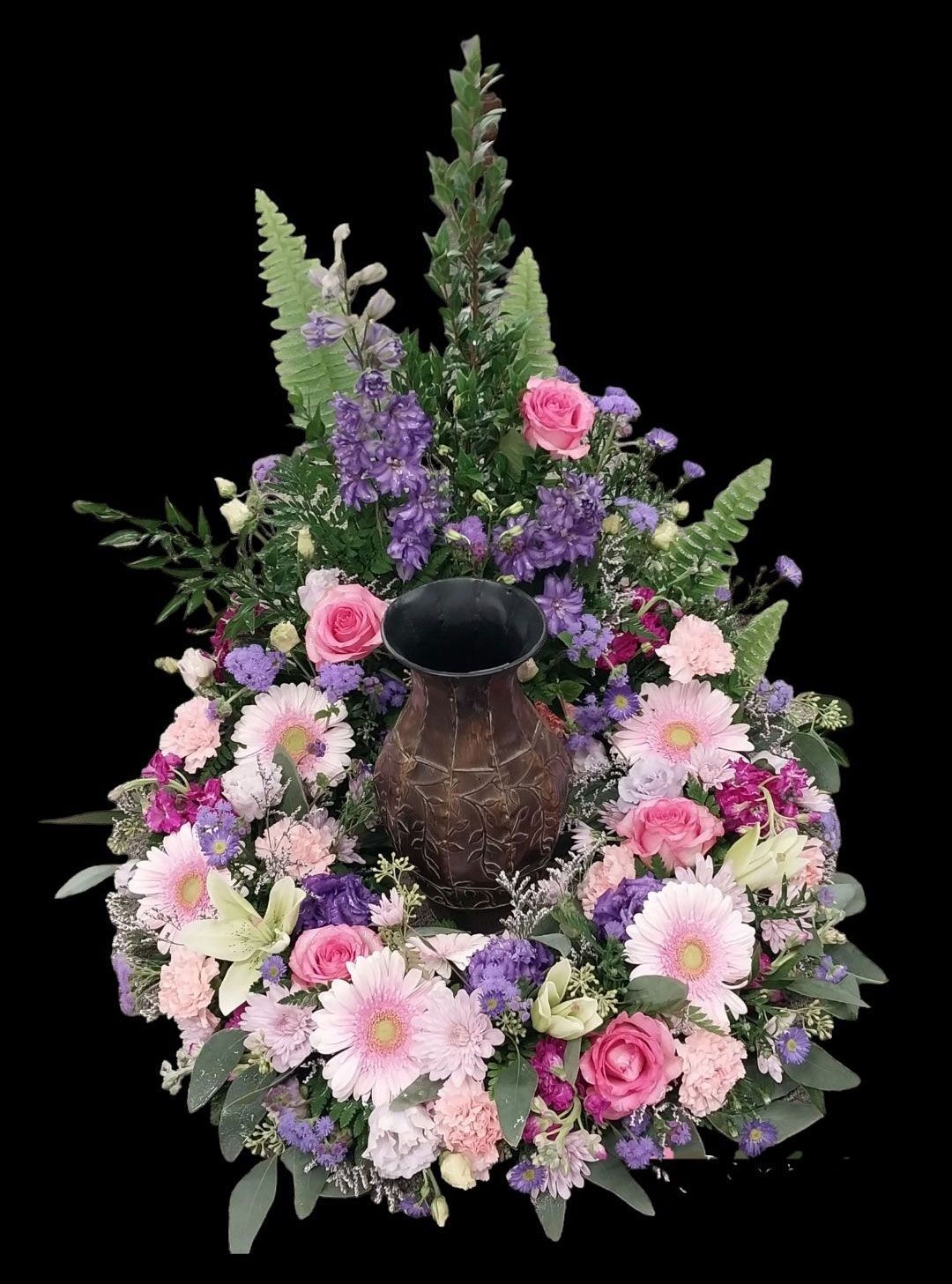 Floral wreath surrounding a brown urn, with pink, purple, and white flowers.