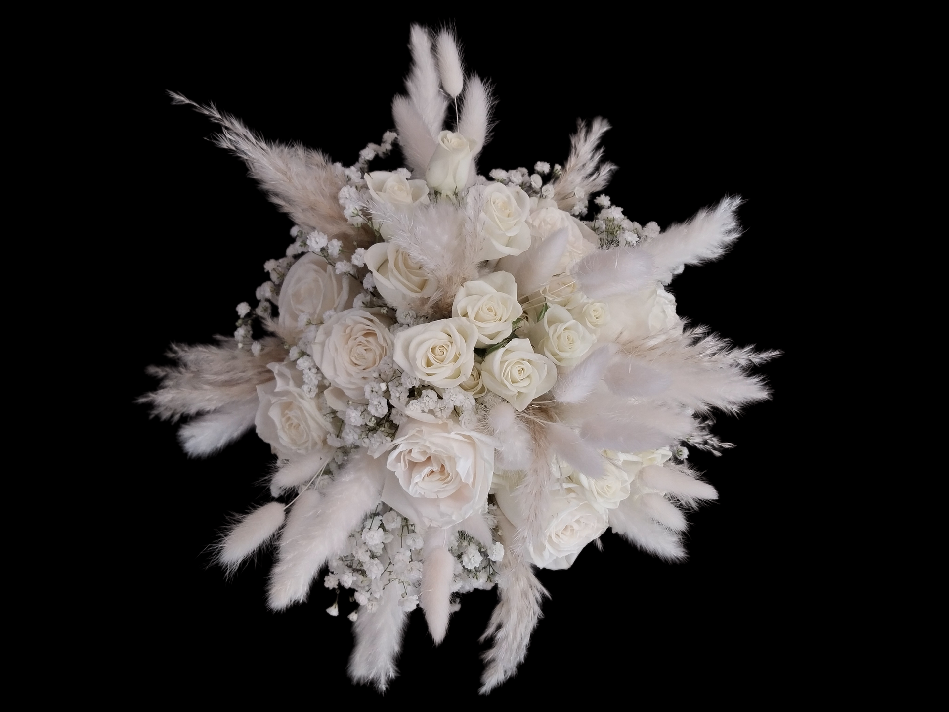 White floral bouquet with roses and pampas grass against a black background.