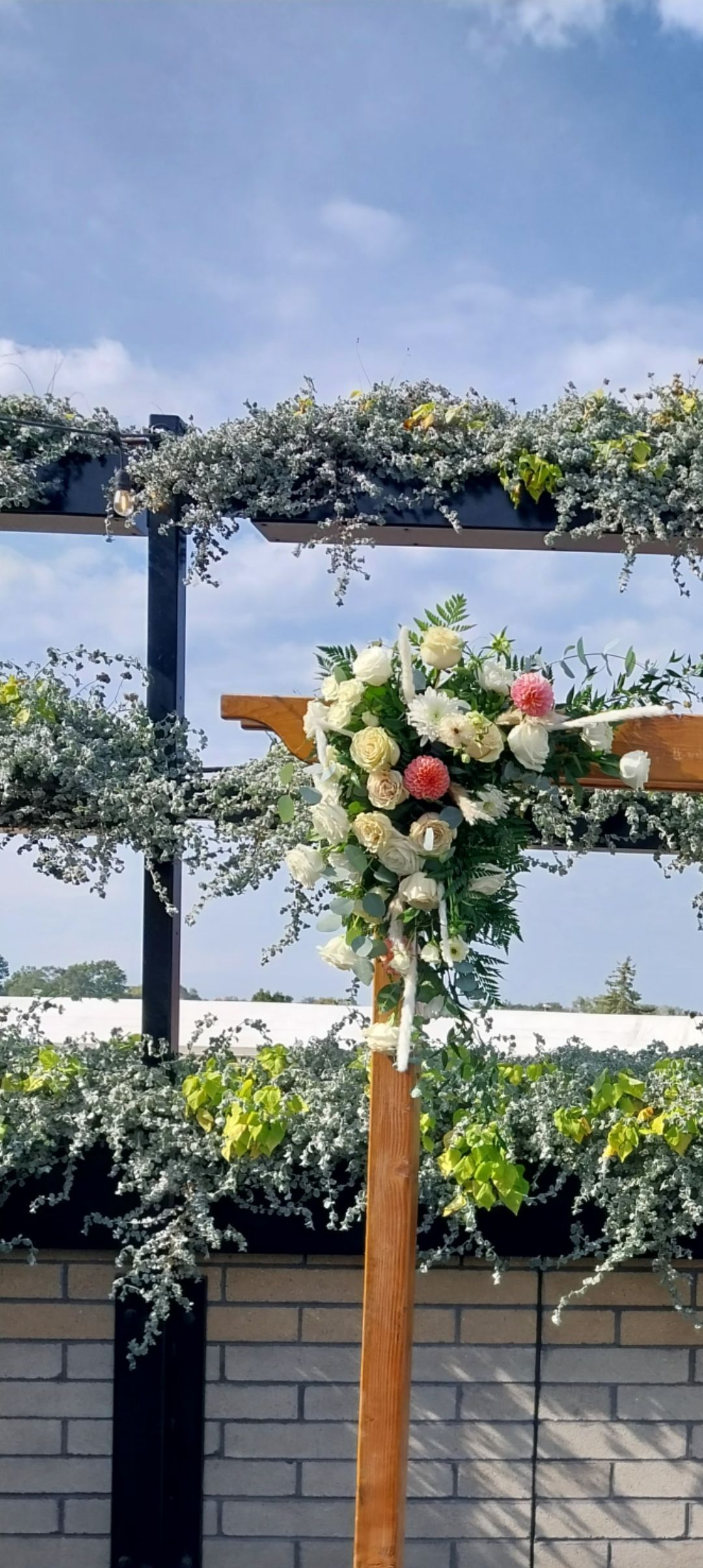 Wedding arbor decorated with flowers and greenery against a blue sky.