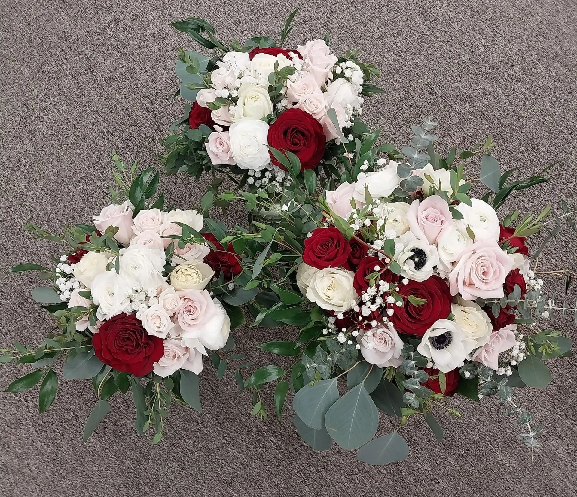 Three bouquets of red, white, and pink roses and greenery on a gray surface.