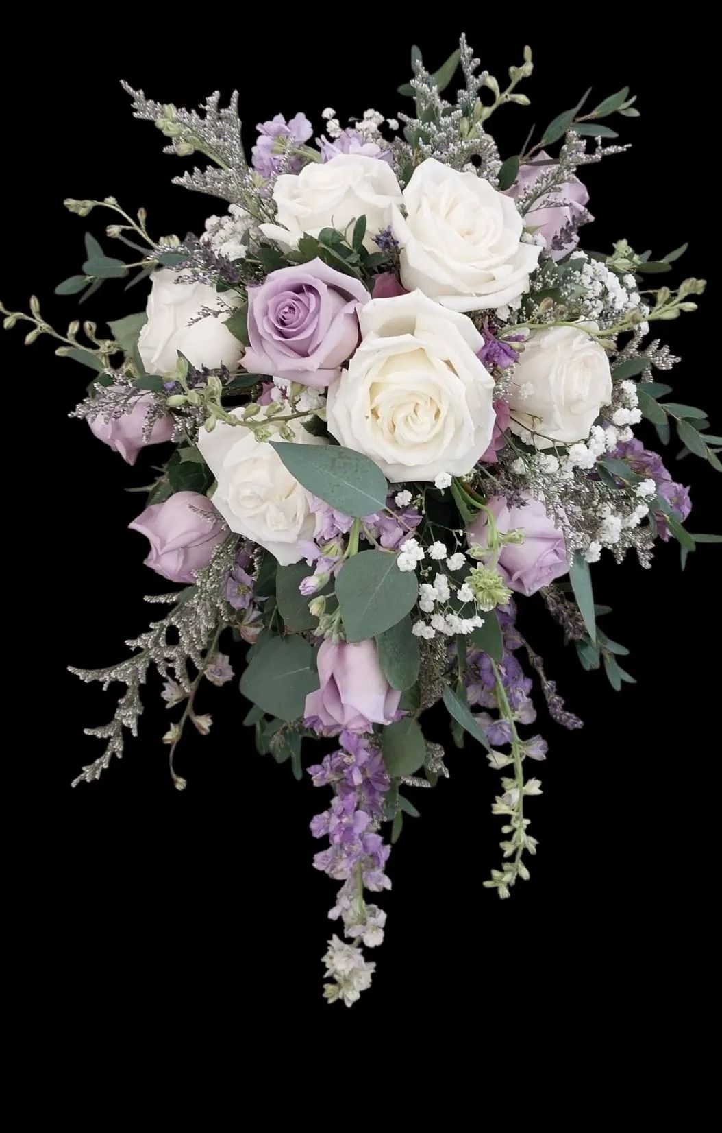 Bridal bouquet of white and lavender roses with cascading greenery against a black backdrop.