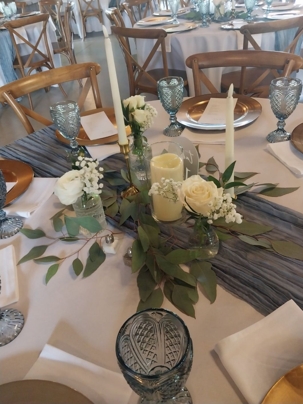 Wedding reception table setting with floral centerpiece, candles, and blue-tinted glassware.