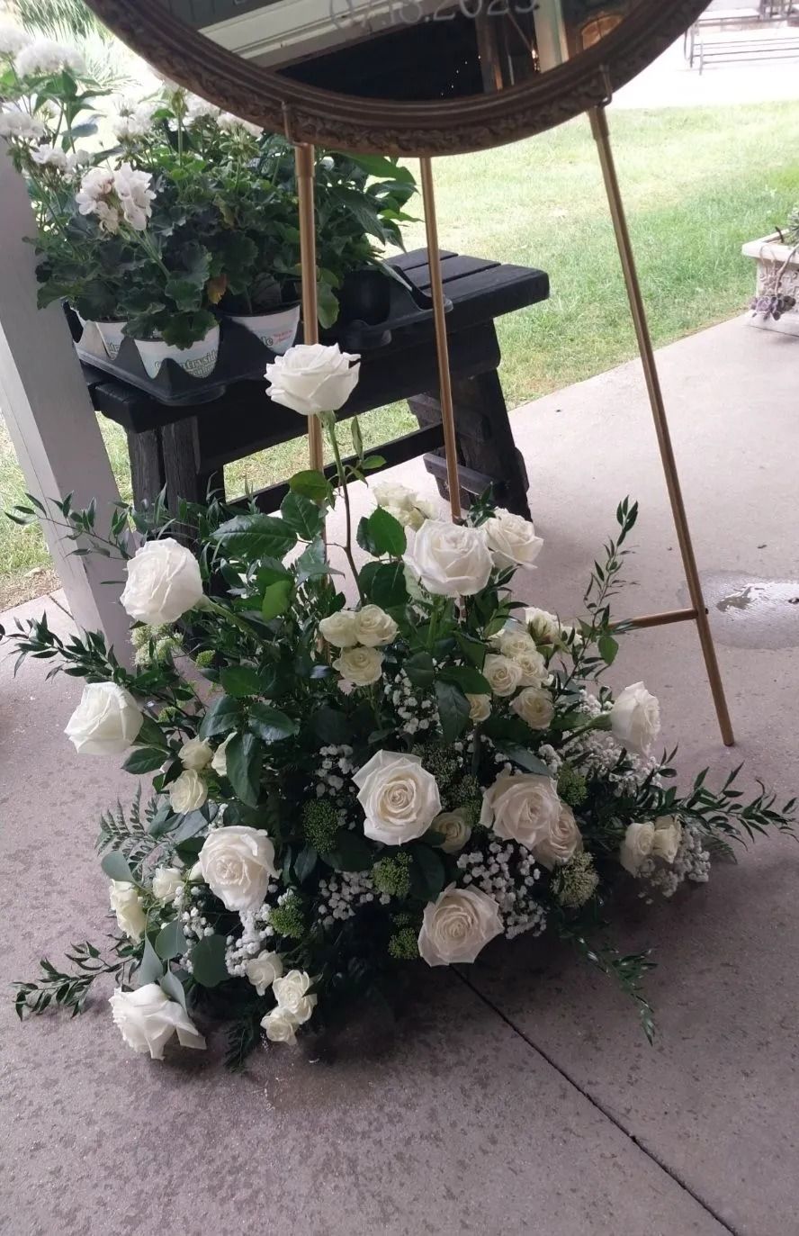 White roses and greenery arranged beneath a gold-framed mirror on a porch.