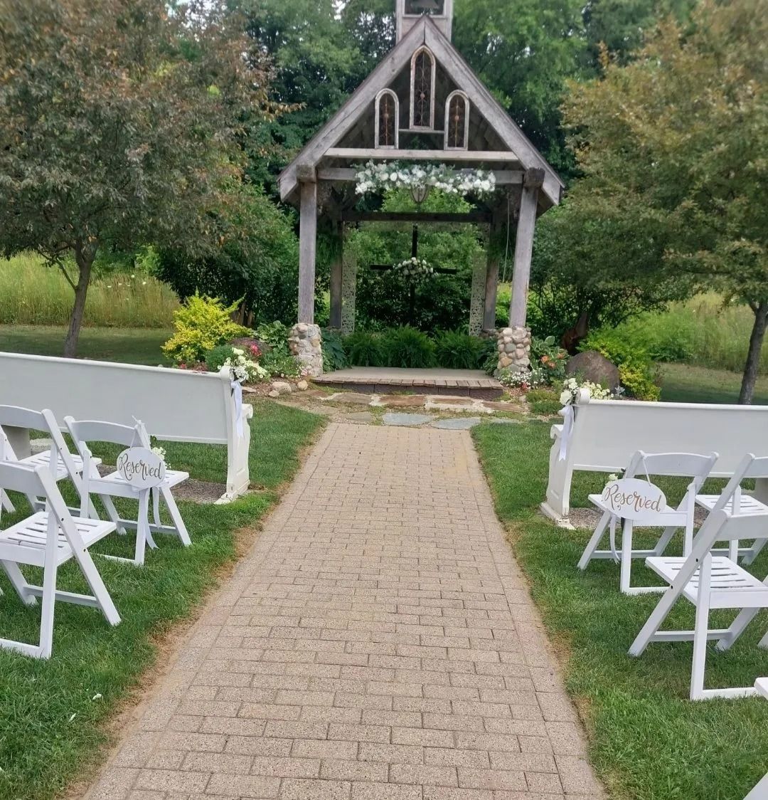 Wedding ceremony setup: white chairs line a brick path leading to an open wooden gazebo decorated with flowers.