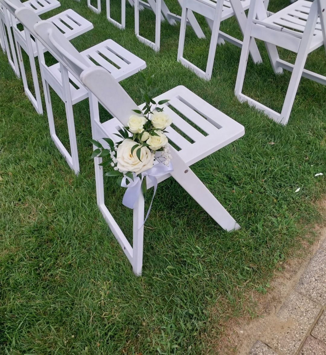 White folding chairs arranged on green grass, one decorated with white flowers and ribbon.