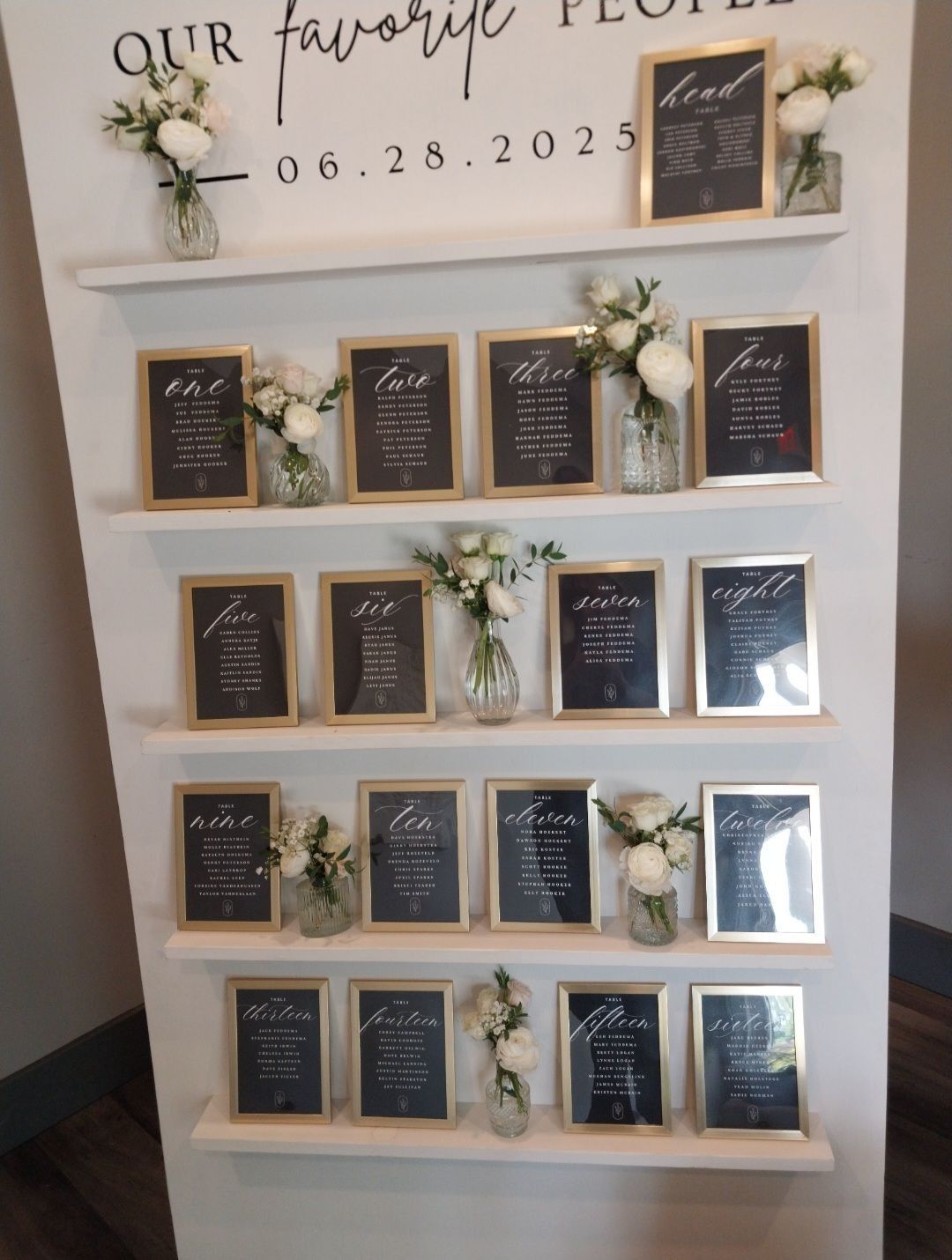 White seating chart with gold frames, black text, white flowers, and the date 