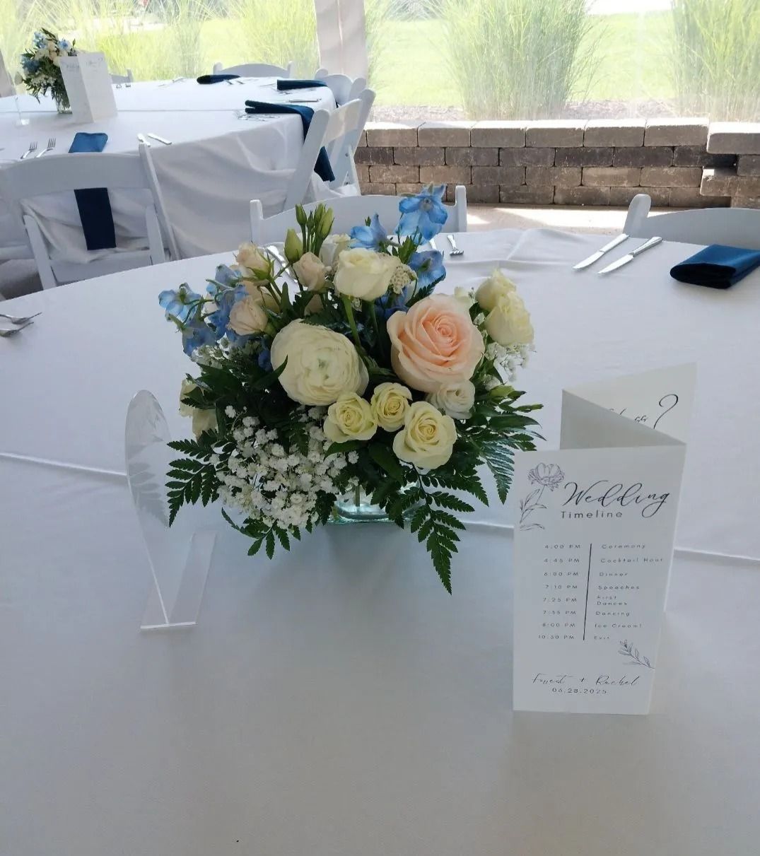 Round table with floral centerpiece and place card at a wedding reception, white tablecloth.
