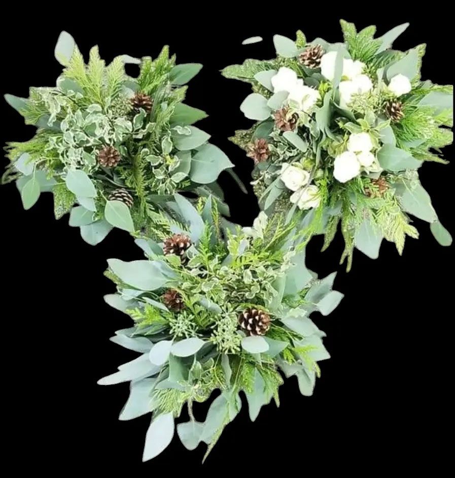 Three bouquets of greenery with pinecones and white flowers, arranged on a black background.