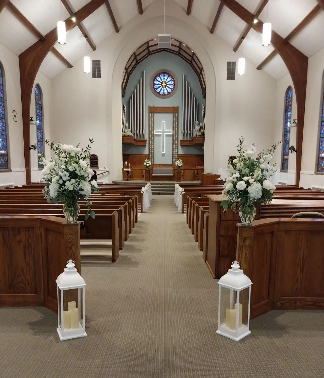 Church interior decorated for a wedding with floral arrangements, lanterns, and empty pews.