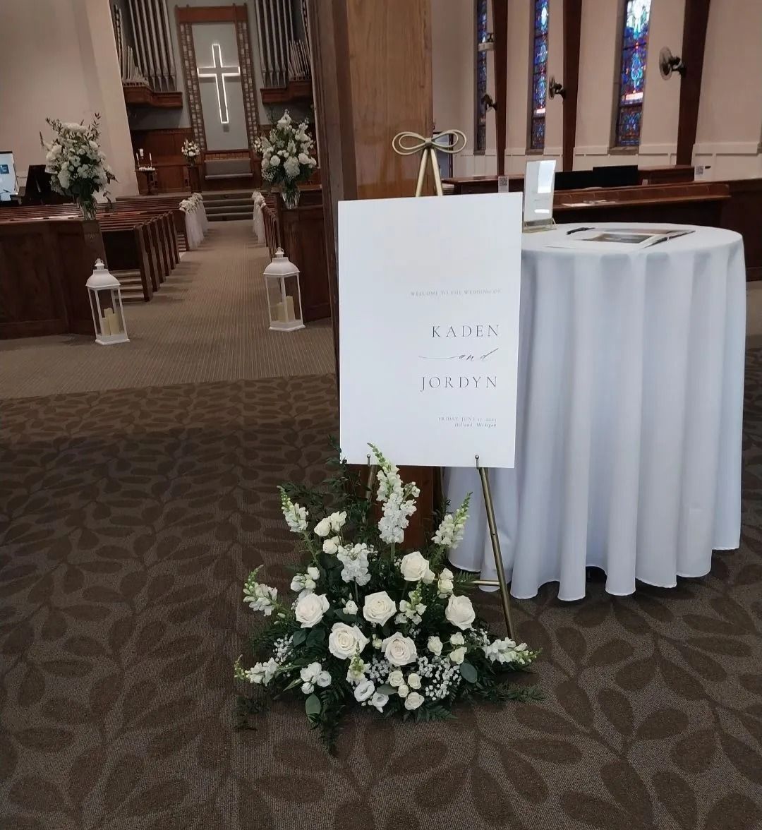Wedding welcome sign with floral arrangement. Church interior with white flowers and sign for Karen & Jordan.