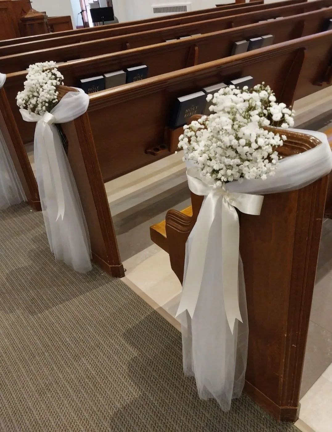 Rows of church pews decorated with white flowers, tulle, and ribbons. Brown wood interior.