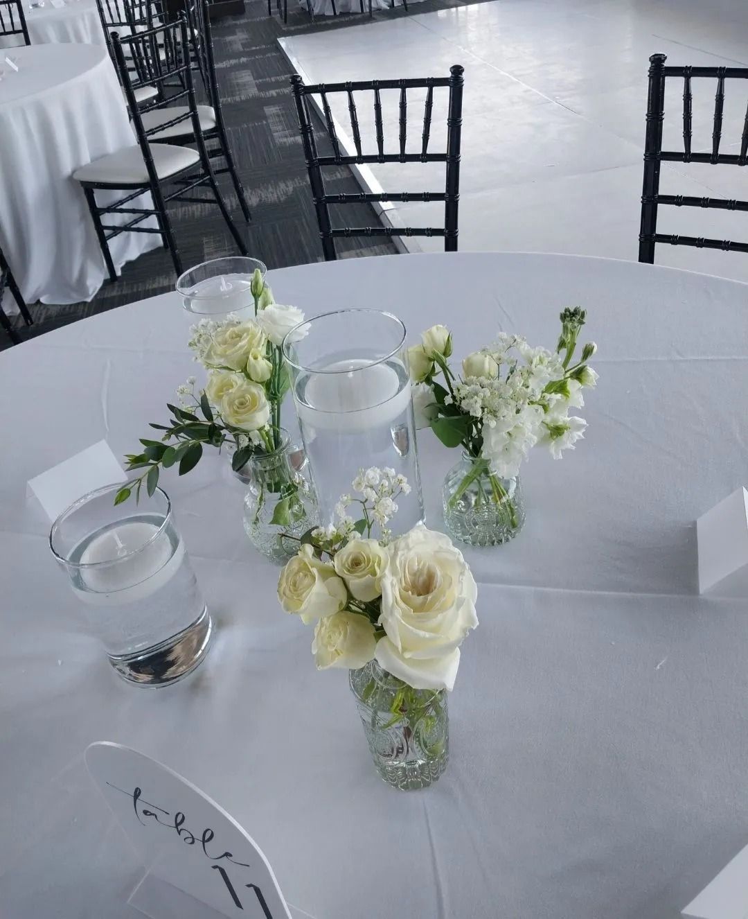 White floral centerpieces on a round table, with black chairs and a light floor in the background.