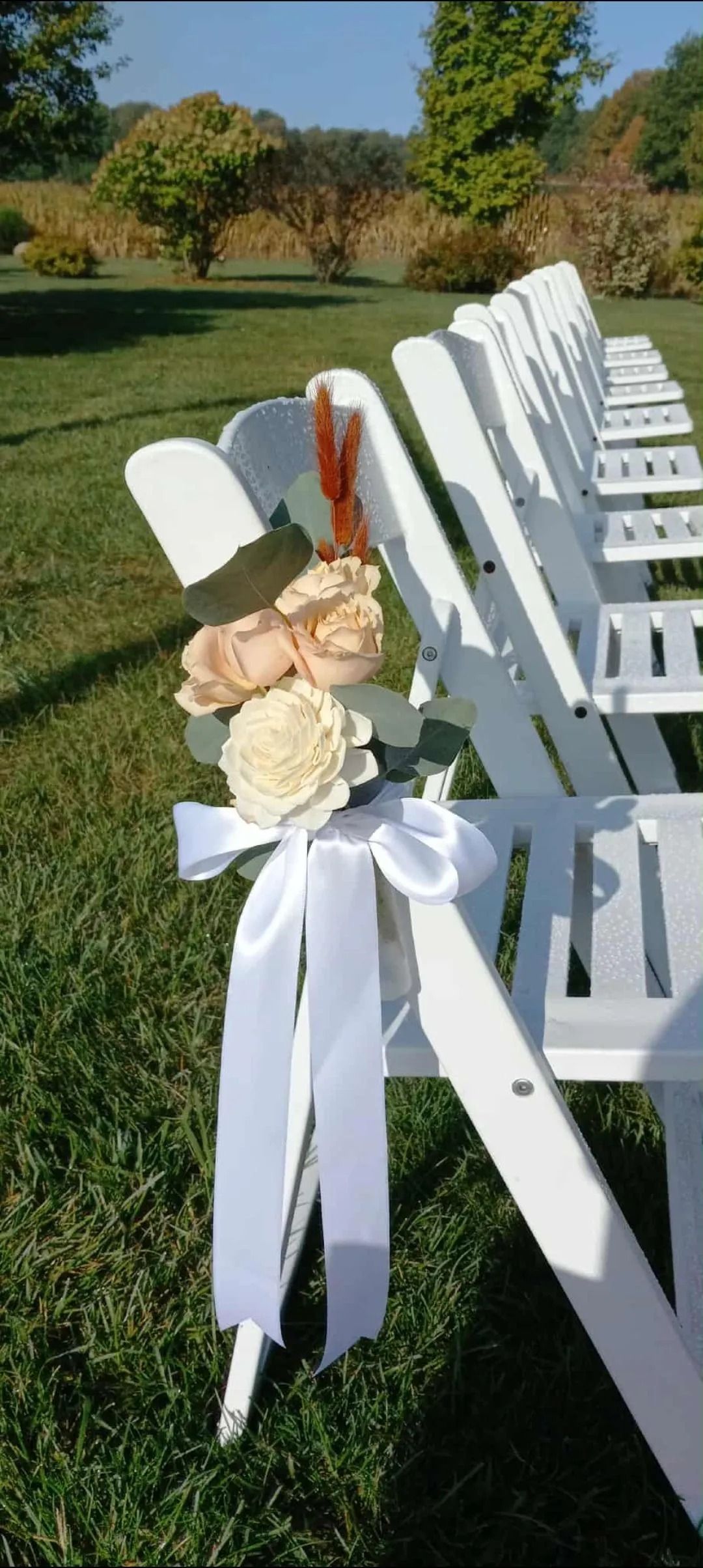White folding chairs decorated with flowers and ribbons sit on a grassy lawn.