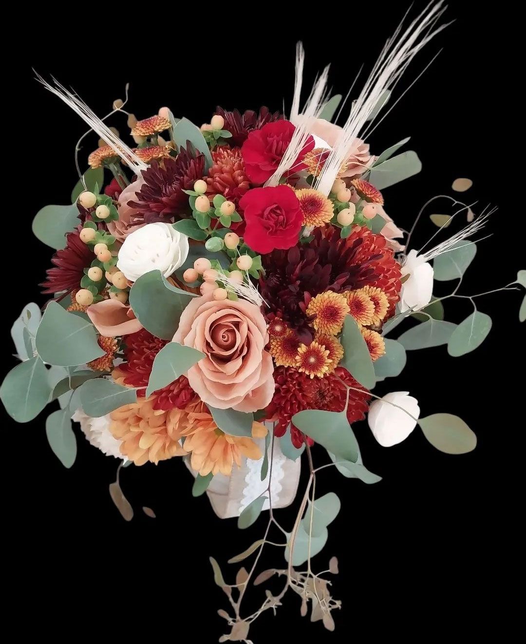 Bouquet with red, orange, and white flowers, eucalyptus leaves, on a black background.
