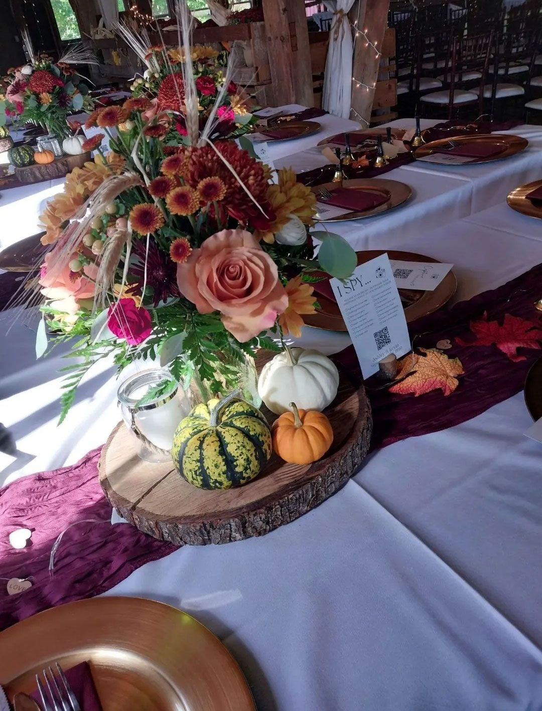 Table setting with fall floral arrangement, pumpkins, and burgundy runner.