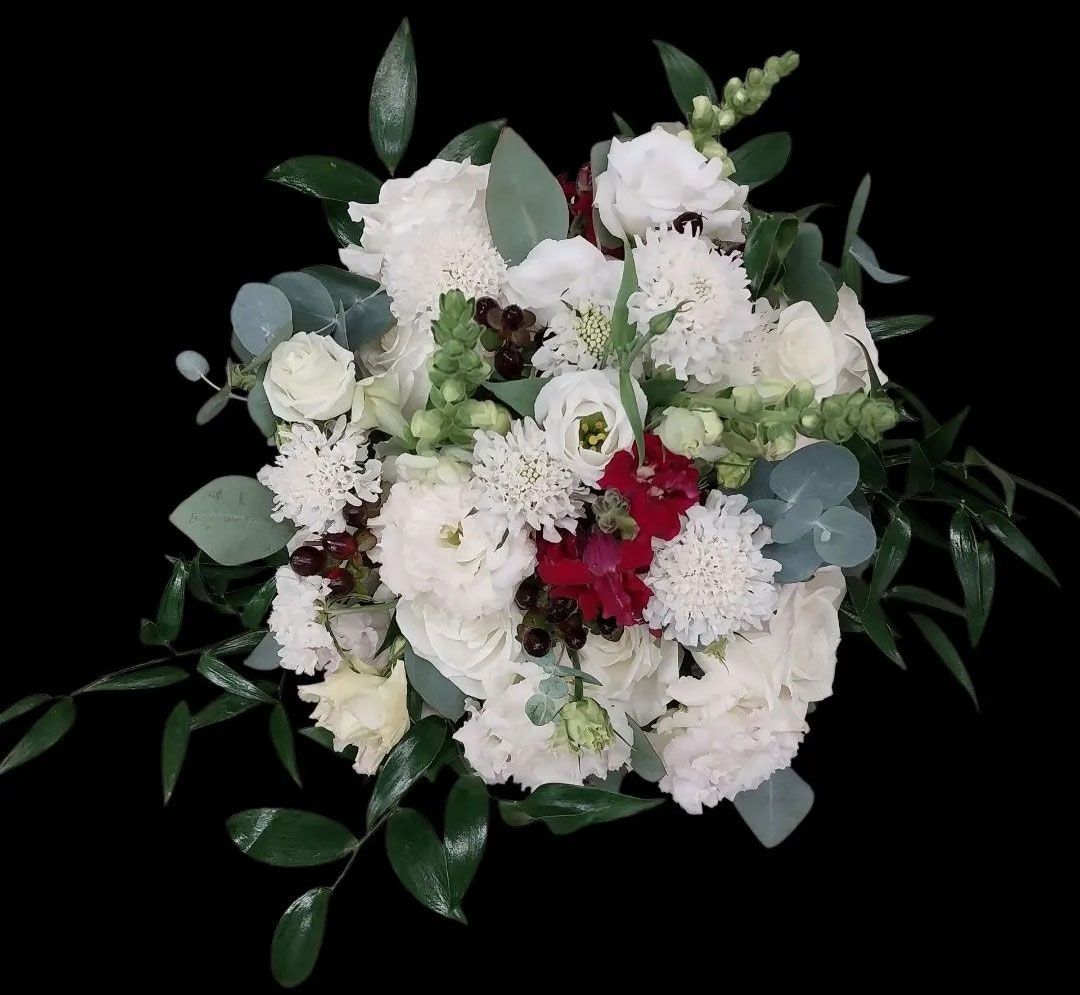 Bouquet of white flowers with green foliage and touches of red, on black background.