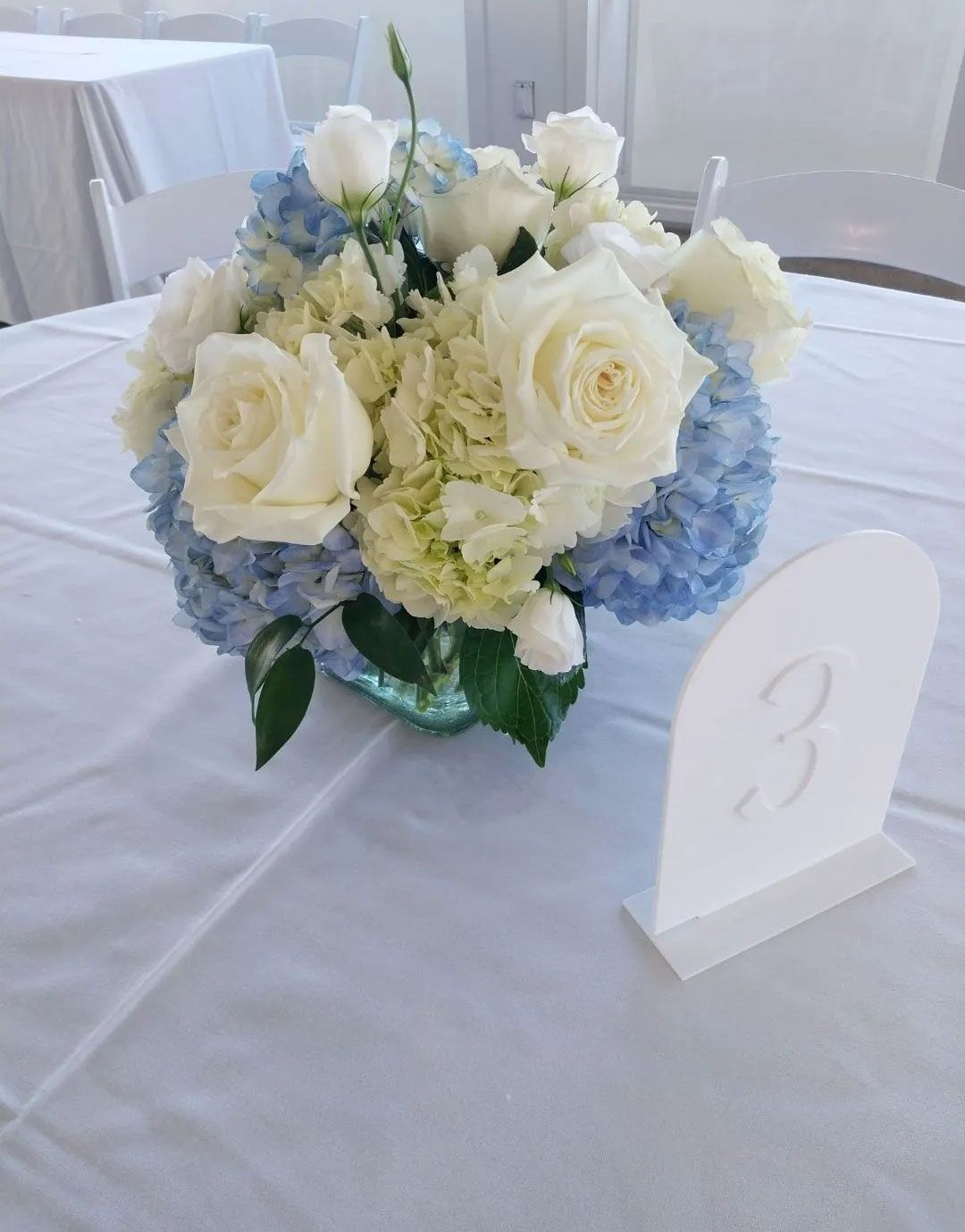Table setting with white tablecloth, flower arrangement, and number 3 table sign.