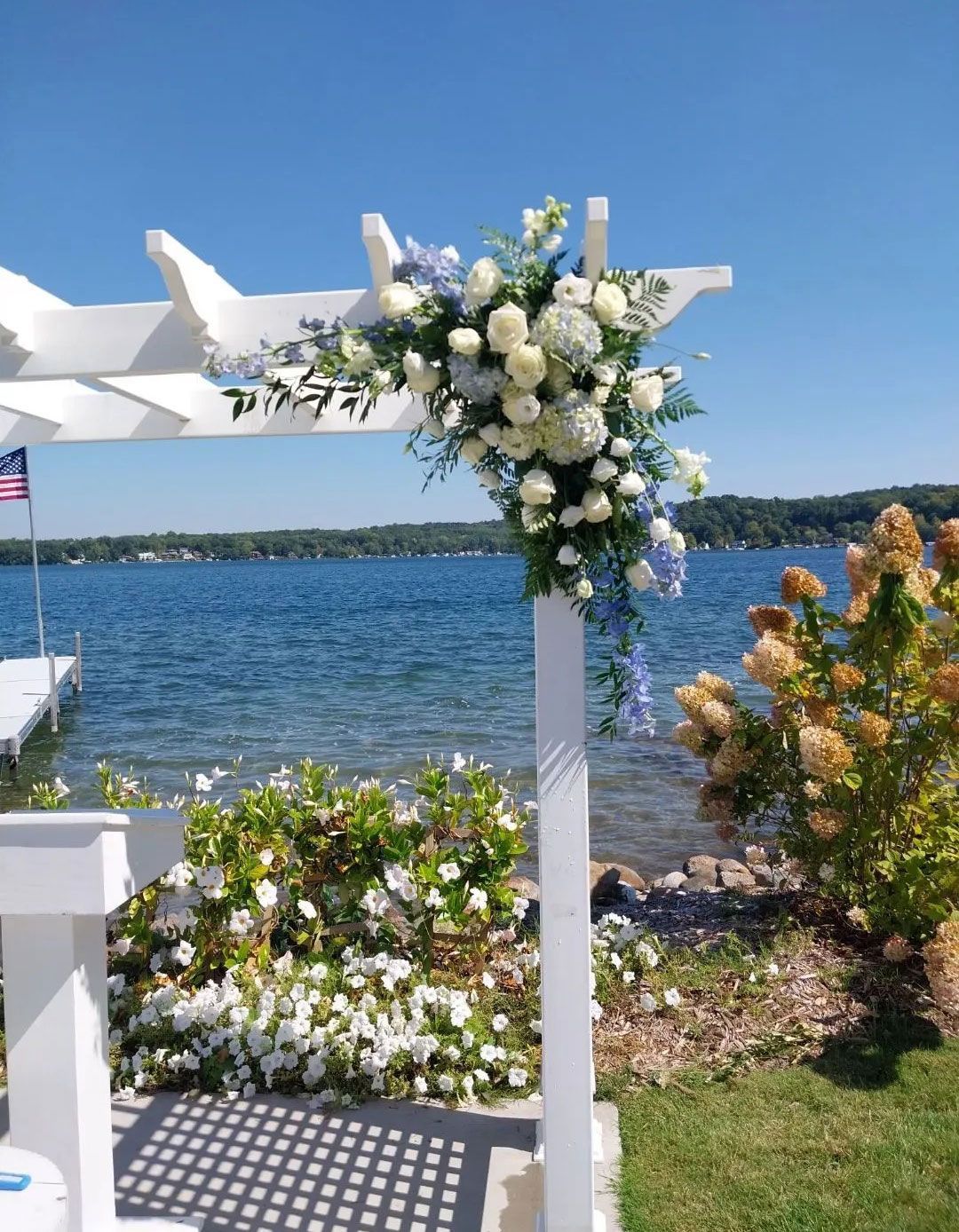 White floral arrangement on a pergola overlooking a lake.