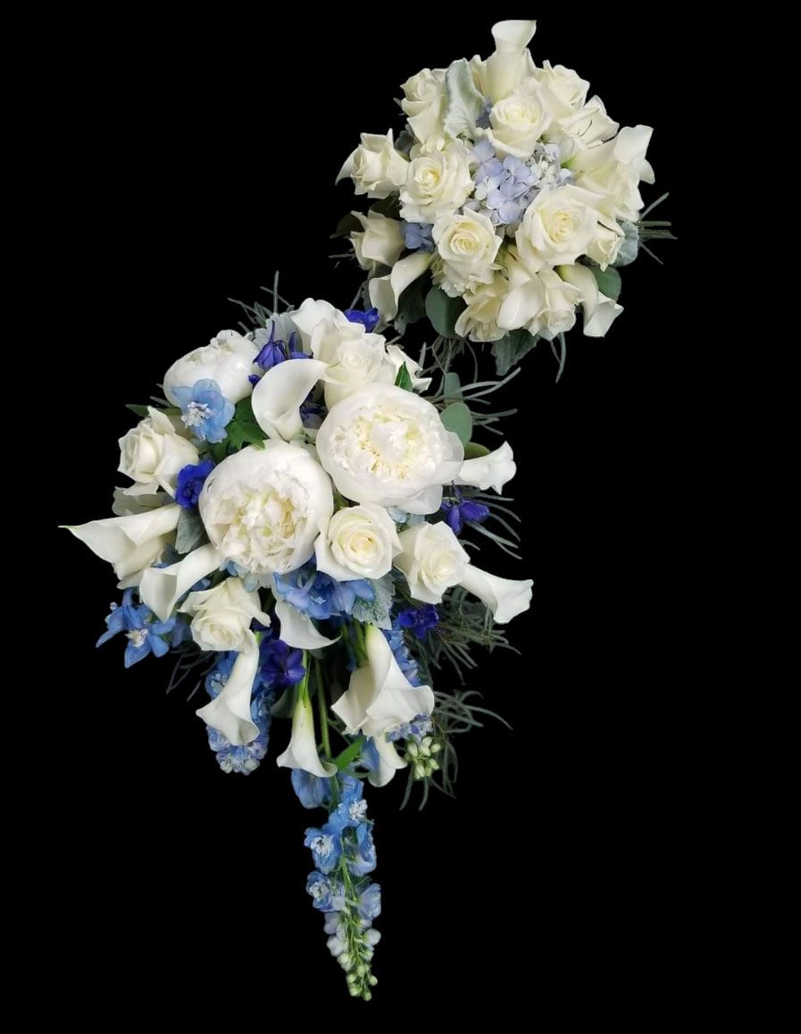 Two bouquets of white roses, calla lilies, and blue delphinium against a black background.