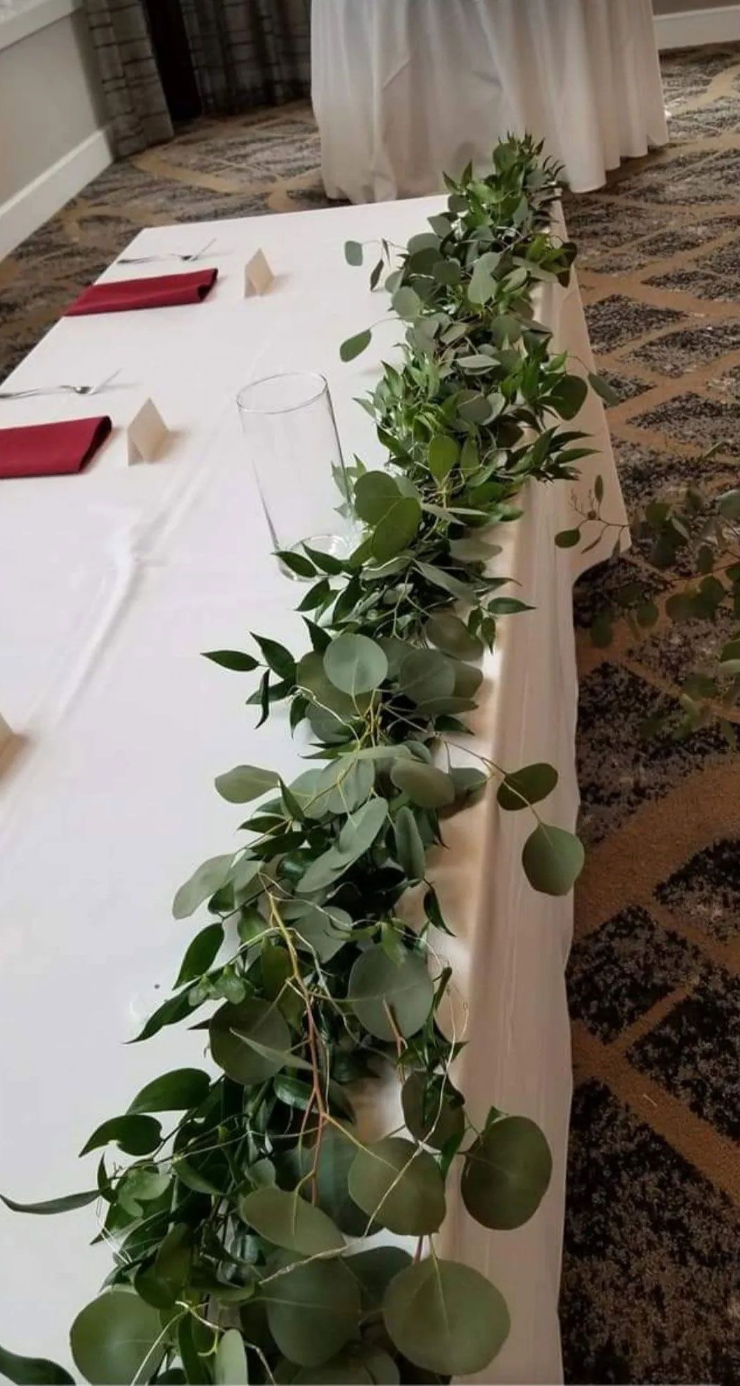 Table decorated with eucalyptus garland for an event, set with red napkins and neutral place cards.