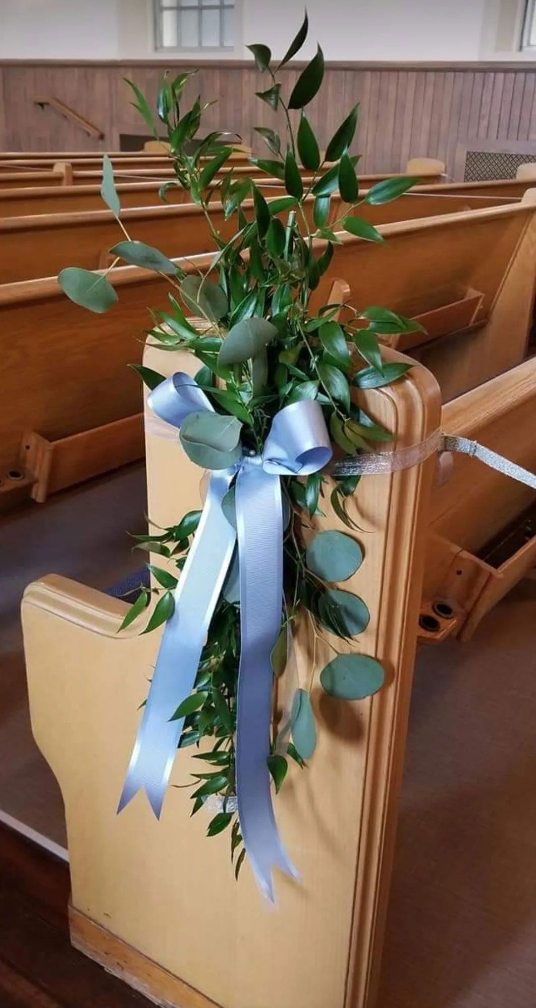 Greenery and blue ribbon decorate a wooden church pew.
