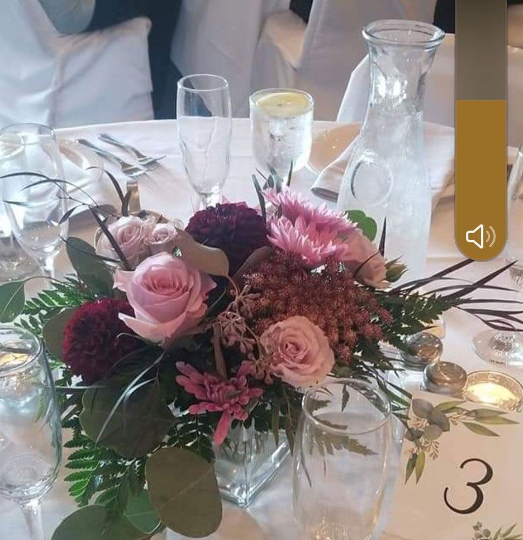 Centerpiece of pink and burgundy flowers on a wedding table set with glassware and a table number.