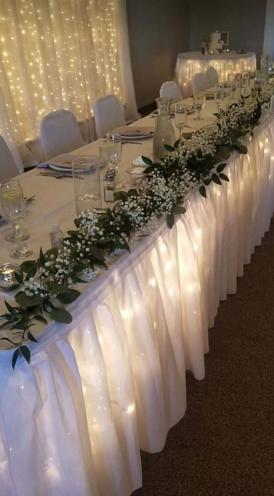 Wedding reception table with white tablecloth, greenery, and fairy lights.