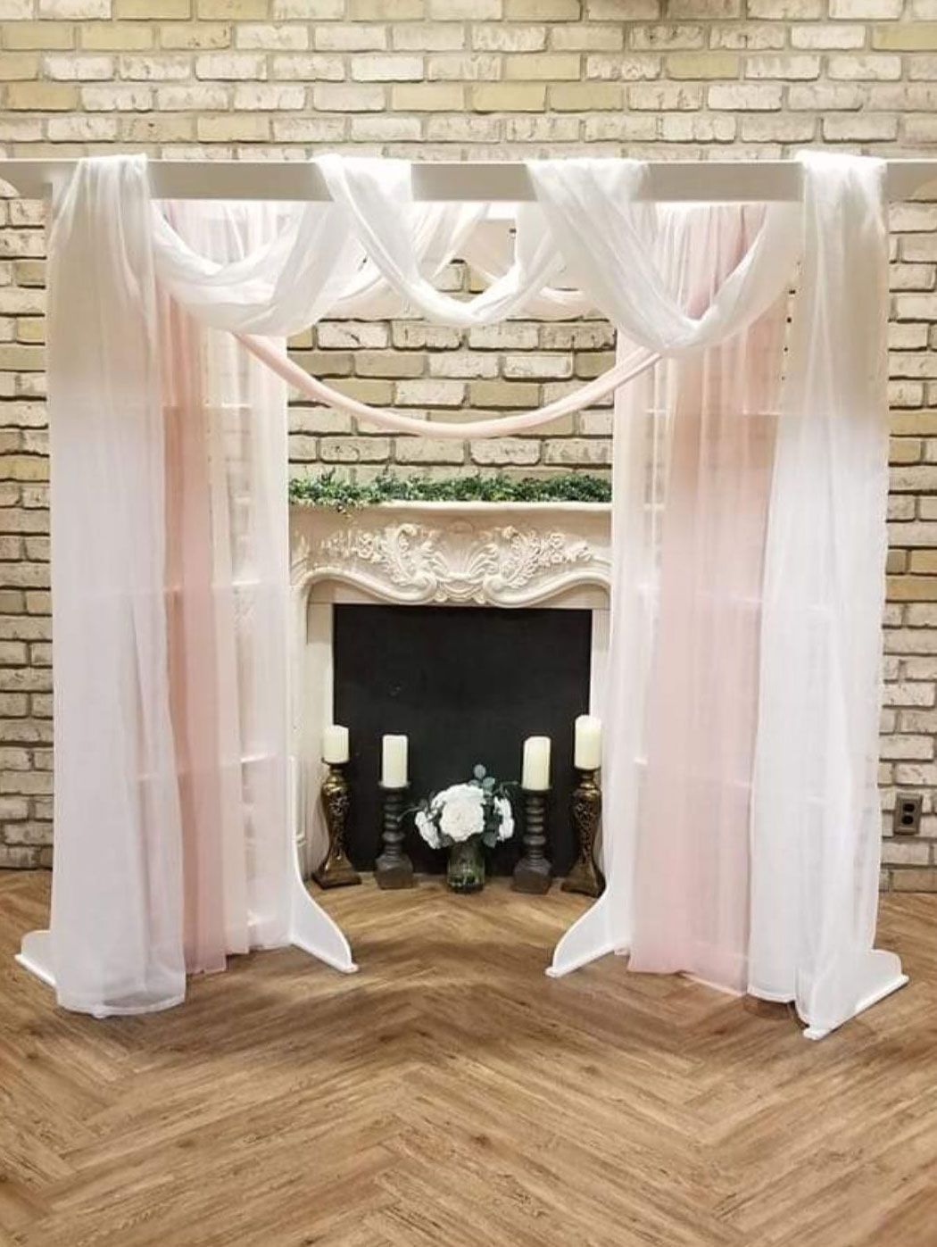 Wedding arch with white and pink draping in front of a fireplace.