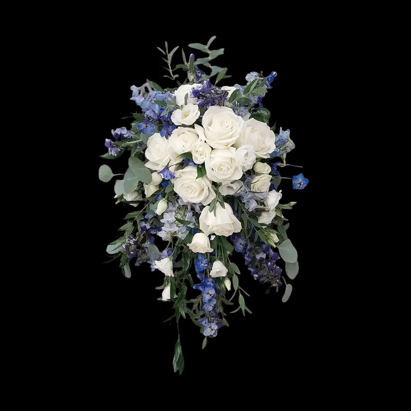 Bouquet of white roses and blue delphinium flowers with green foliage against a black background.