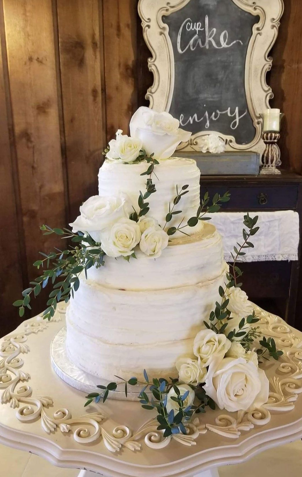 Three-tiered white wedding cake with floral accents and gold trim on a decorative cake stand.