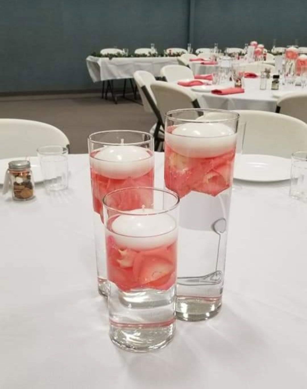 Three clear glass vases with floating candles and pink fruit on a white tablecloth.