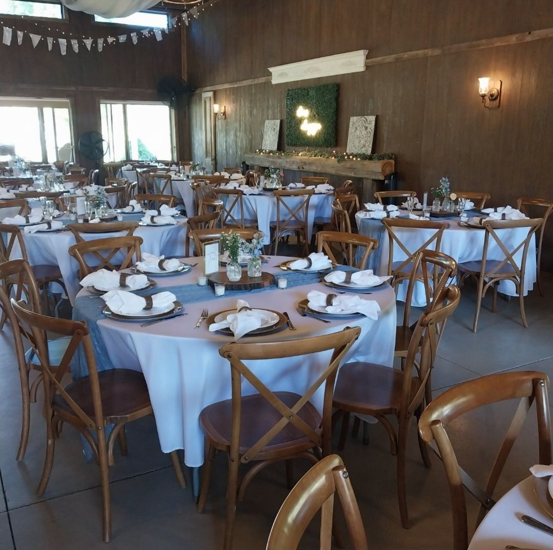 Wedding reception hall with round tables, white tablecloths, and wooden chairs.