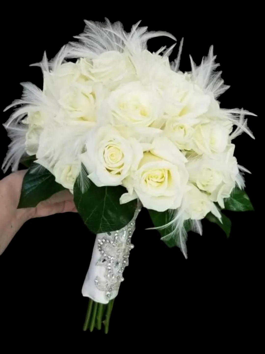 White rose bouquet with feathers and jeweled handle, held by a hand.
