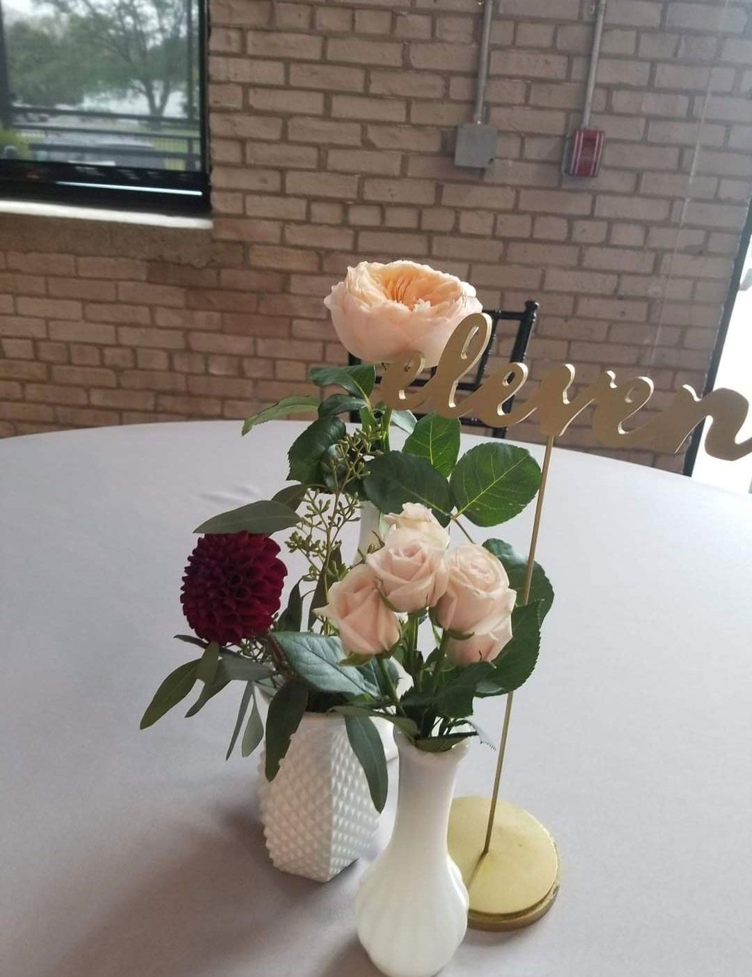 Floral centerpiece on a round table, featuring roses, greenery, and a 