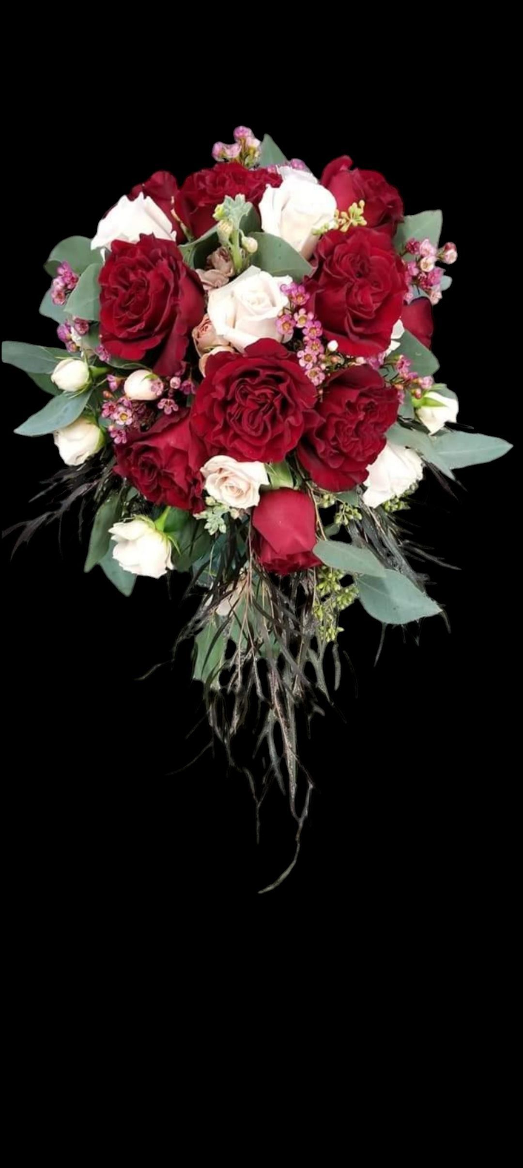 A cascading bridal bouquet with burgundy and white roses, greenery, and dried grasses against a black background.
