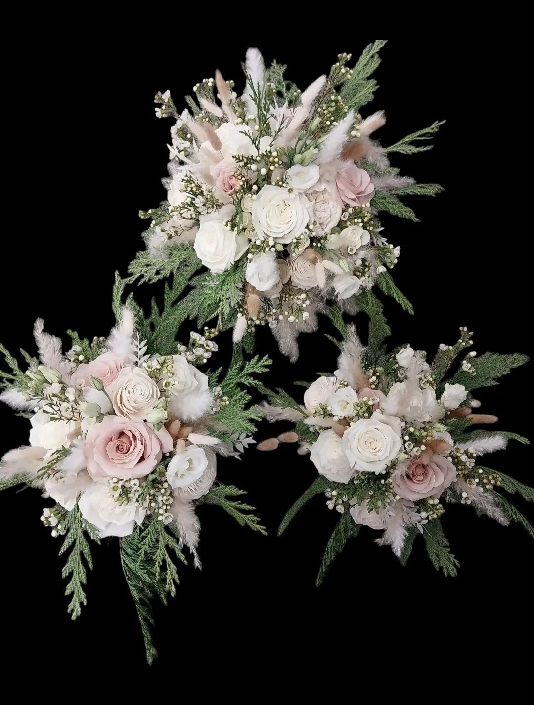 Three bouquets of white and blush roses with fluffy beige accents and greenery against a black background.
