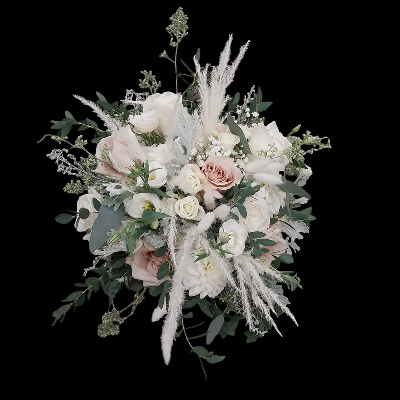 Bridal bouquet with white and dusty rose flowers, pampas grass, and greenery against a black background.