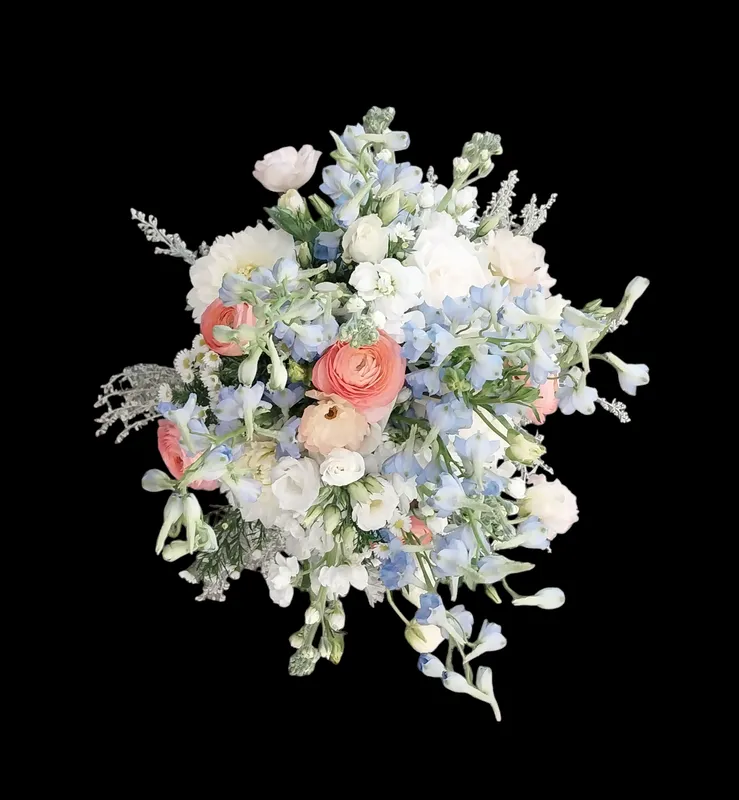 Bouquet of pastel flowers: pink ranunculus, blue delphinium, white blossoms, and greenery.