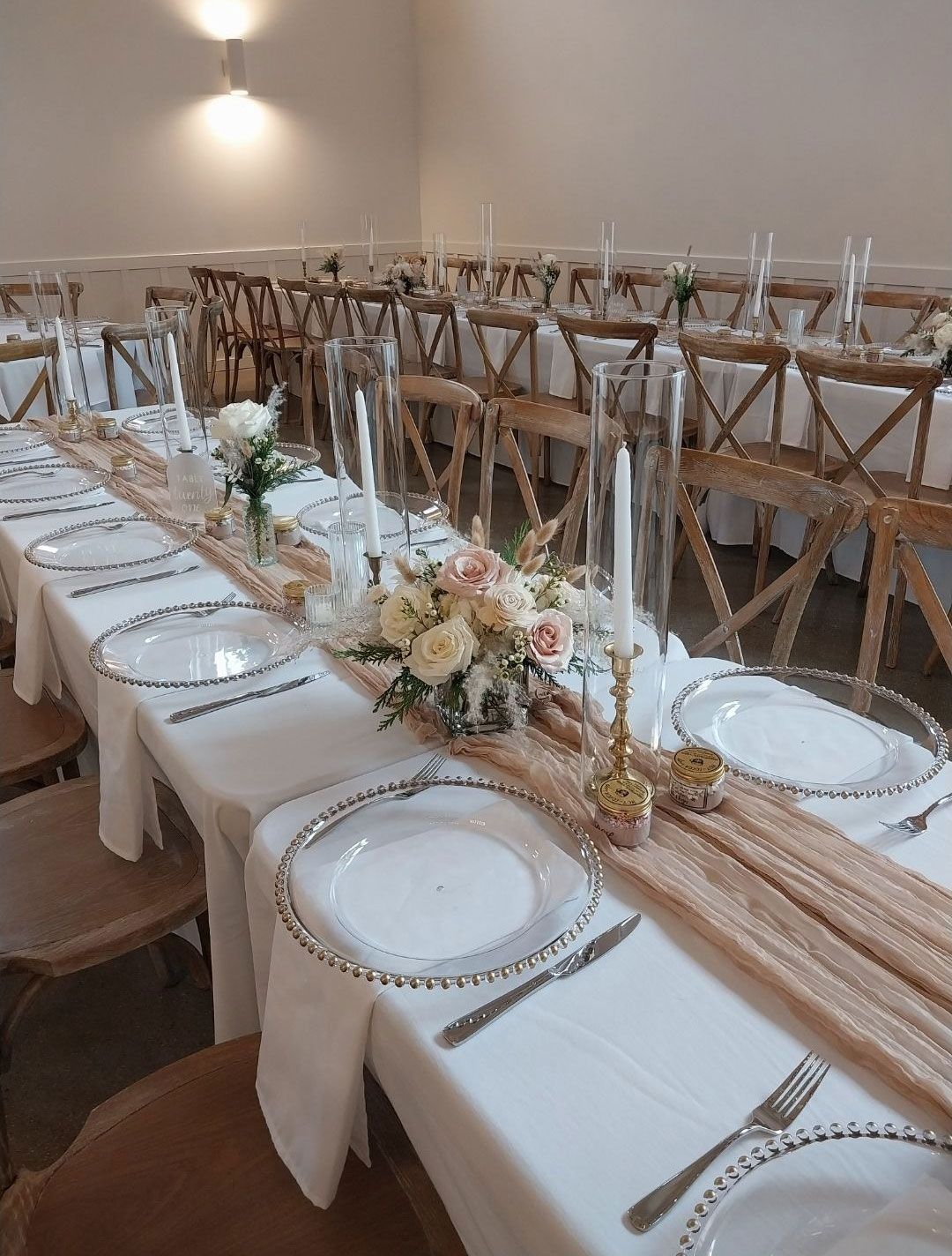 Wedding reception table setting with floral arrangements, candles, and cross-back chairs.