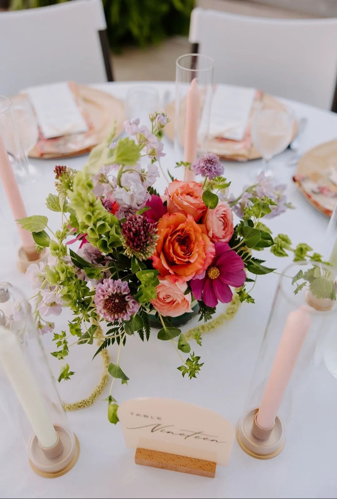 A floral centerpiece with orange roses on a table setting. Pink and green accents, elegant decor.