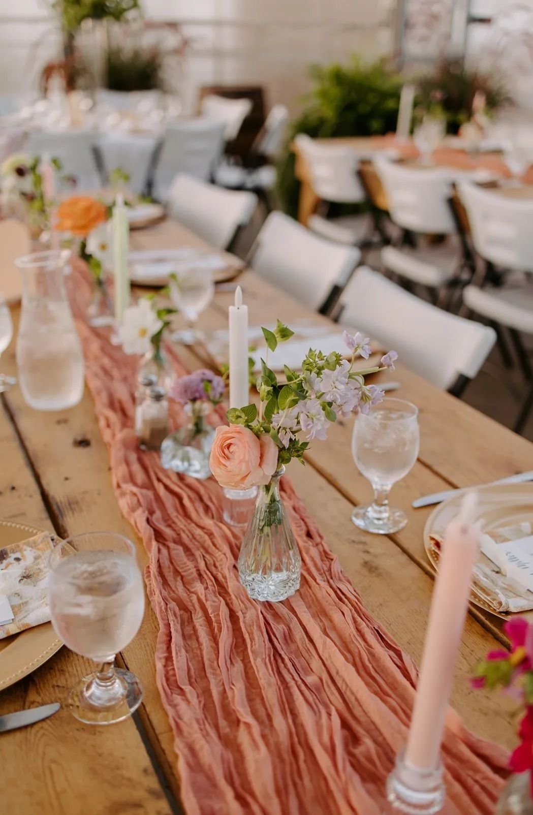 Wooden table set for a wedding, with a terracotta runner and floral centerpieces.