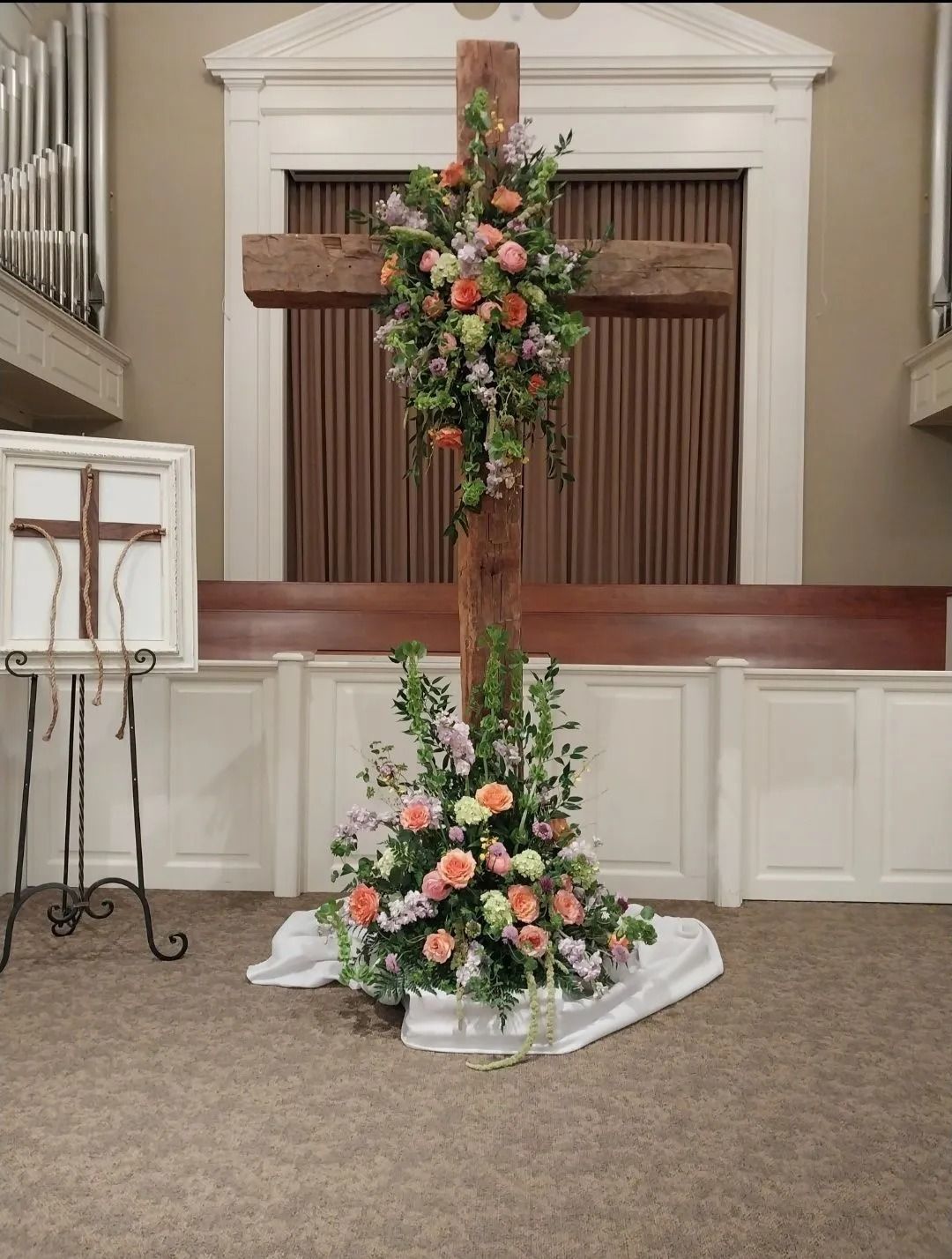 Wooden cross adorned with flowers in a church. Another small cross on an easel to the left.